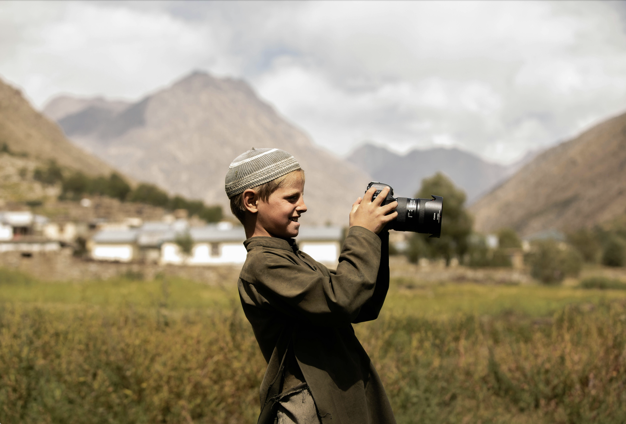 Image of a boy standing in a valley in Afghanistan looking into the viewer of a large professional camera.